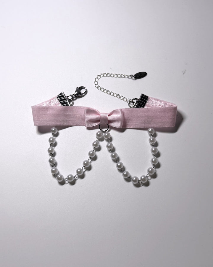 A pink satin bow anklet with dangling pearl strands, silver-tone chain extender, on a plain light background.
