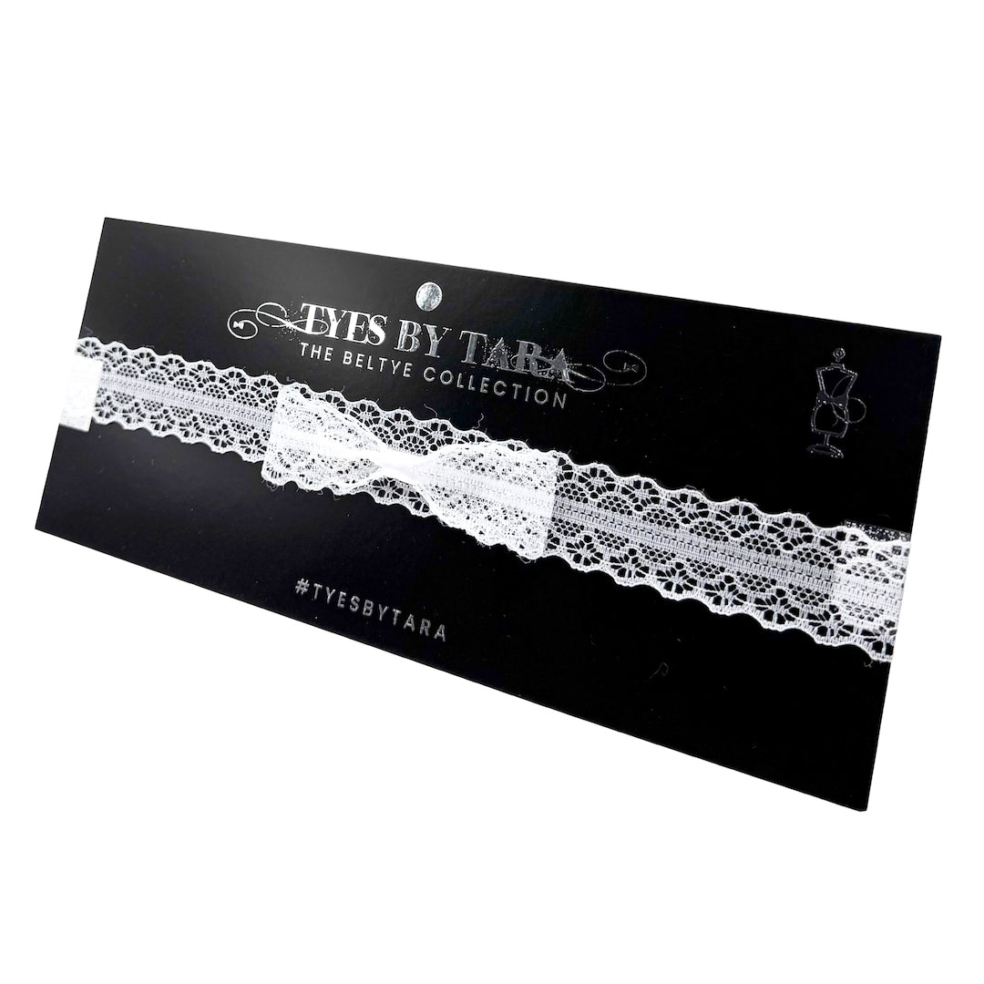 An white lace bow belt with adjustable strap, packaged on a black card with the brand name 'TYES BY TARA' written in elegant script.