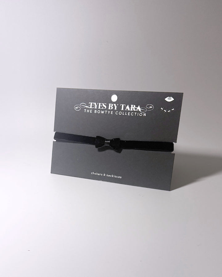 A black velvet bow choker displayed on a black branded card from Tyes By Tara, set against a plain light gray background.