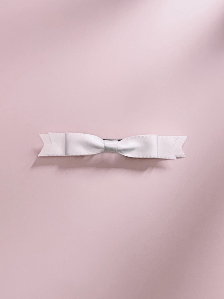White satin hair bow french barrette on a pink background