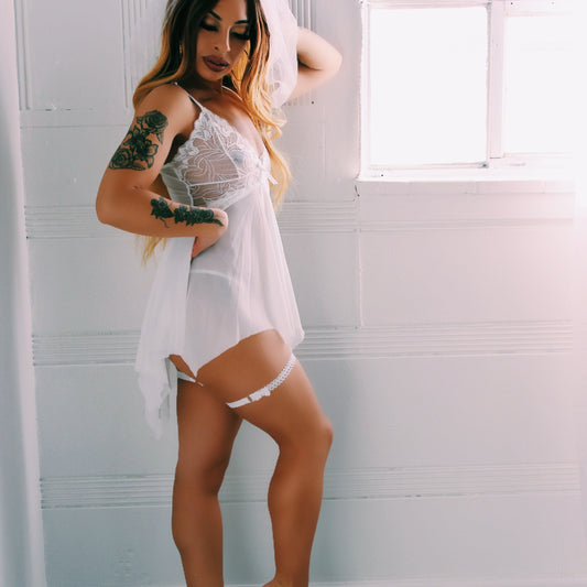 Woman in a white lace nightgown standing in a room with white walls and a window with Lady White Leg Garters