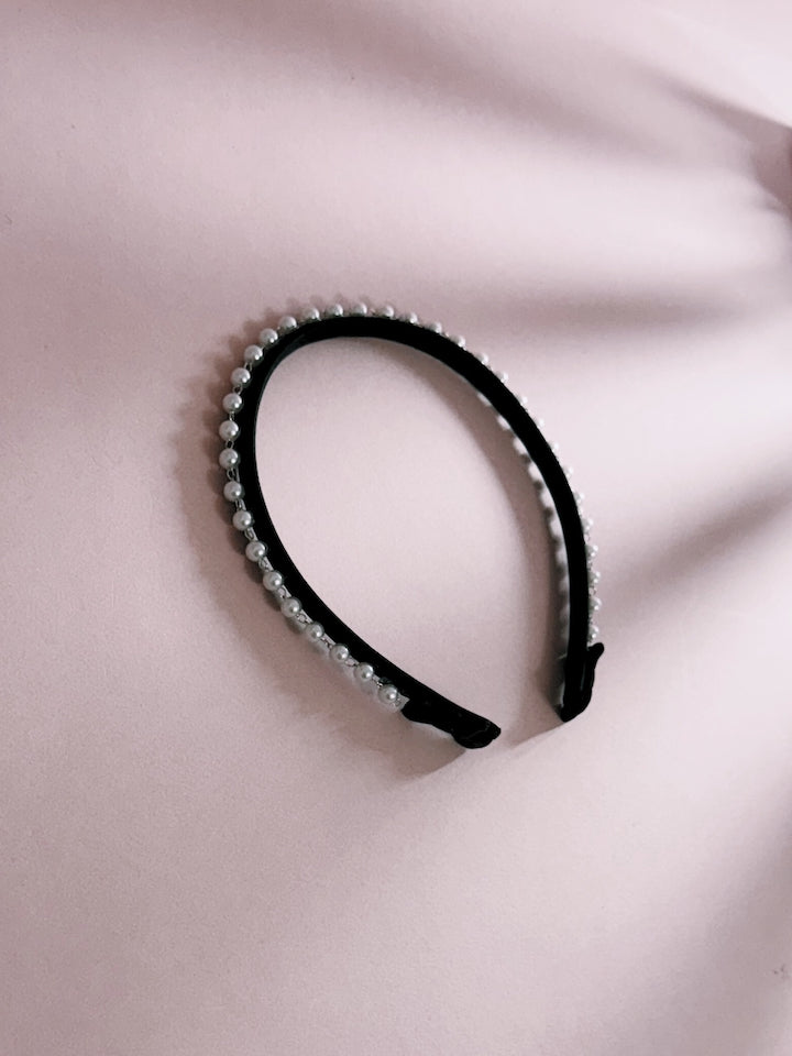 Pearl Headband. A black headband with pearl-like embellishments on a light pink fabric background