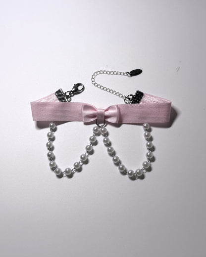 A pink satin bow anklet with dangling pearl strands, silver-tone chain extender, on a plain light background.