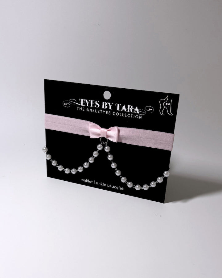 Light pink bow anklet with pearl chain drape displayed on black card 