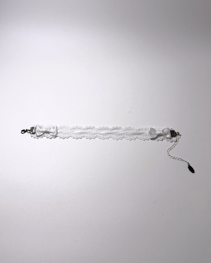 A white lace anklet with satin bow details and silver-toned metal hardware, photographed against a plain light gray background.