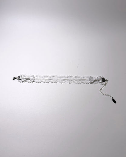 A white lace anklet with satin bow details and silver-toned metal hardware, photographed against a plain light gray background.