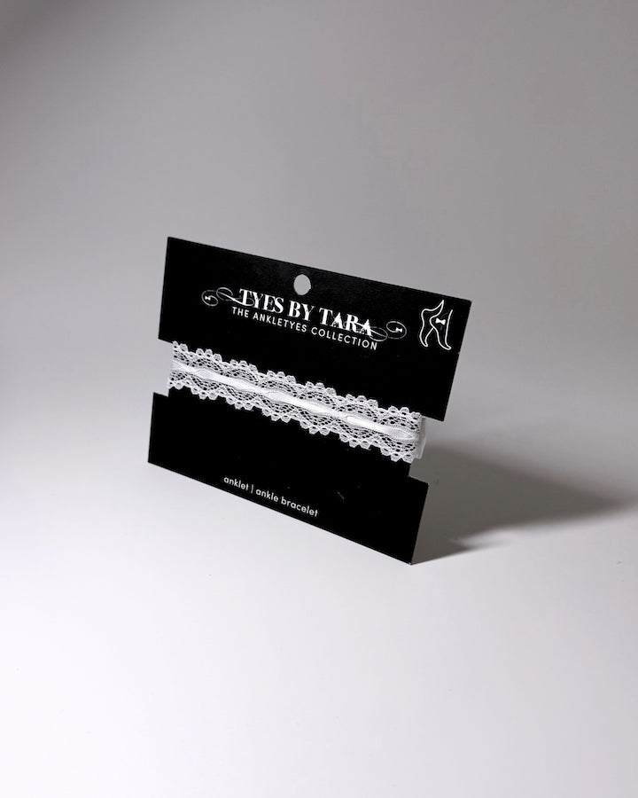 White anklet lace displayed on a black retail card labeled 'TYES BY TARA THE ANKLETYE COLLECTION' against a light gray studio background.