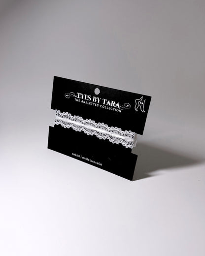 White anklet lace displayed on a black retail card labeled 'TYES BY TARA THE ANKLETYE COLLECTION' against a light gray studio background.