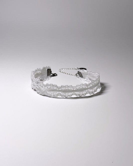 A white lace anklet with white bows with silver-tone metal clasps and a short extender chain, photographed on a plain light gray studio background