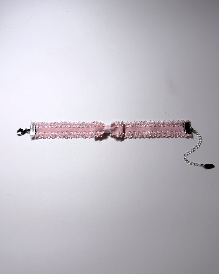 A pink elastic bow anklet with bow centered on the anklet lying flat with silver extender chain and clasp on a softly lit background