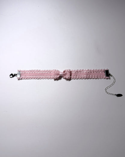 A pink elastic bow anklet with bow centered on the anklet lying flat with silver extender chain and clasp on a softly lit background