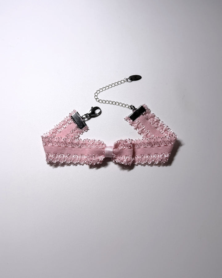 A pink elastic bow anklet with bow centered on the anklet with silver extender chain and clasp on a softly lit background