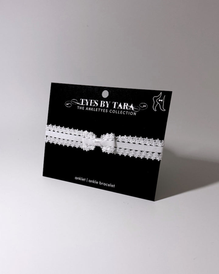 Lady White Elastic Bow Anklet displayed on black card on softly lit background