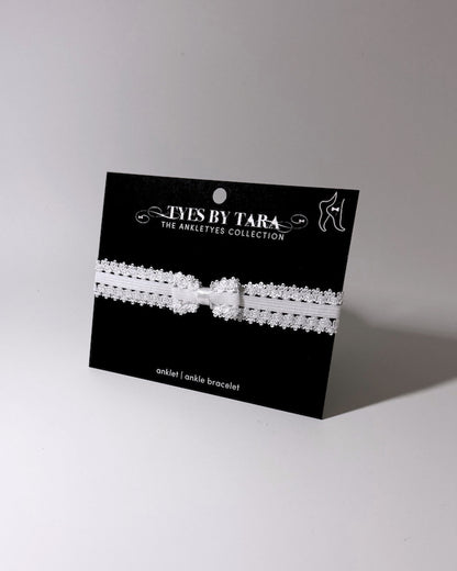 Lady White Elastic Bow Anklet displayed on black card on softly lit background