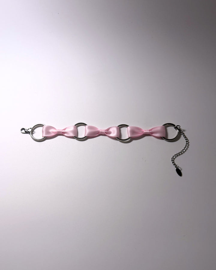 A pink satin anklet with silver-tone metal rings, a lobster clasp, and an adjustable chain extender, laid flat on a light gray background.