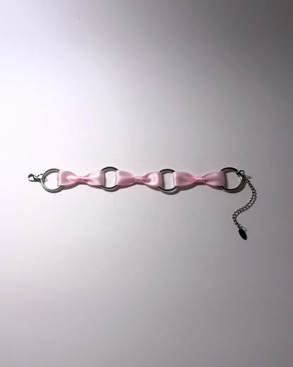 A pink satin anklet with silver-tone metal rings, a lobster clasp, and an adjustable chain extender, laid flat on a light gray background.