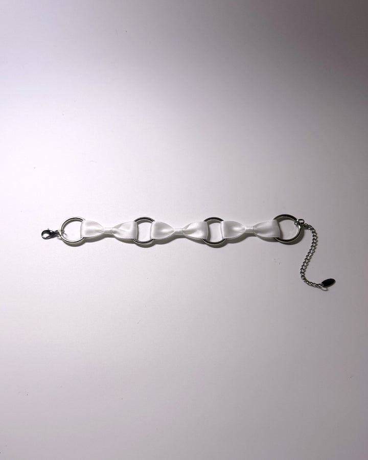 A white satin anklet with silver-tone metal O-rings, a lobster clasp on one end, and a short silver chain extender on the other, displayed on a light gray background.