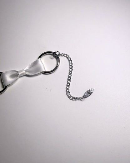 A close-up of a silver-toned metal extender chain and oval tyes by tara logo tag on a plain light background.