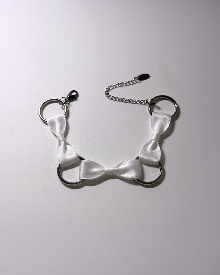 A white bow anklet featuring three white satin bow accents and a silver chain extender with a clasp, displayed on a light gray background.