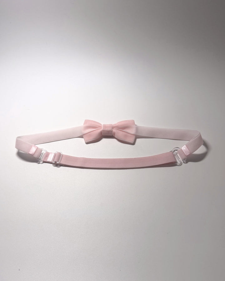 A light pink bow belt showing adjustable strap on softly lit surface