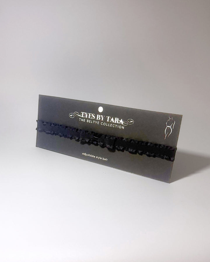 Black Ruffled Bow Belt displayed on black card on softly lit surface 