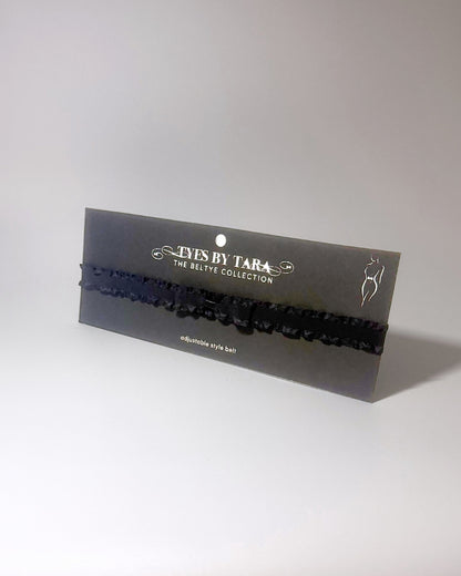Black Ruffled Bow Belt displayed on black card on softly lit surface 