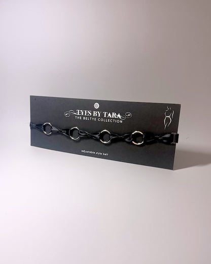 A black bow belt with silver o rings on a black retail card