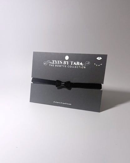 A black velvet bow choker displayed on a black branded card from Tyes By Tara, set against a plain light gray background.