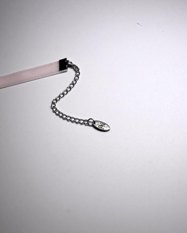 A close-up of a silver chain extender with an oval engraved TYES BY TARA tag on a plain light gray background.