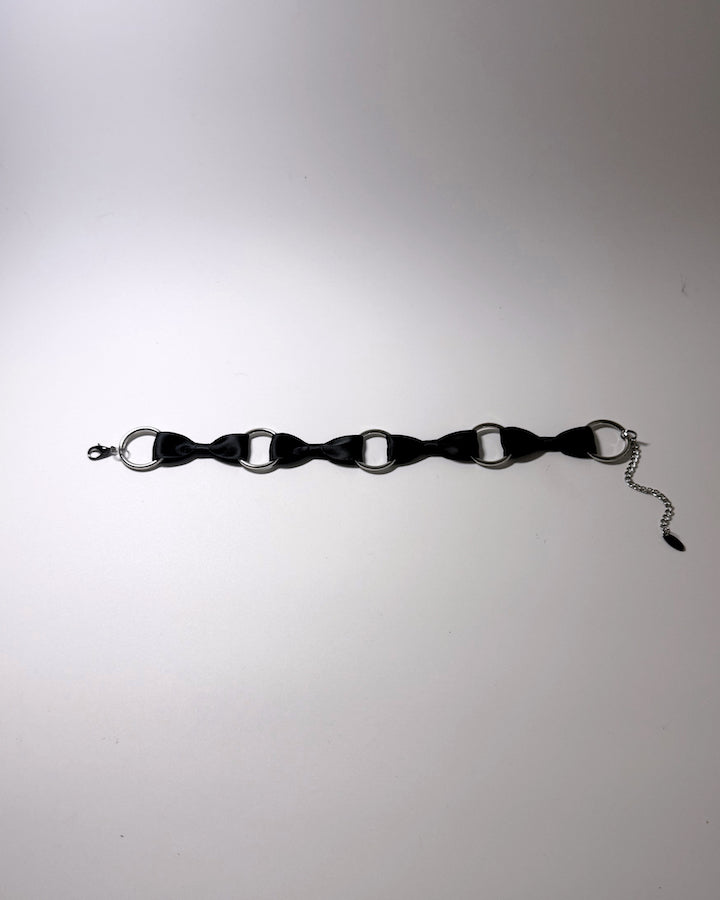 A black satin choker collar with silver-tone metal O-rings, a lobster clasp, and an adjustable chain extender, laid flat on a light gray background.