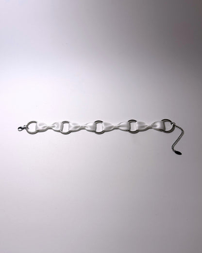 A white bow choker with silver-toned metal O-rings and a silver chain extender, laid flat on a light gray background.