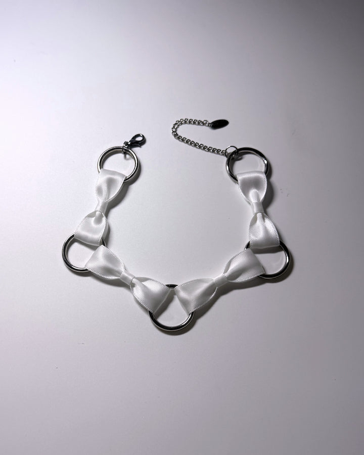 A white satin bow collar with silver metal O-rings and a silver chain extender, displayed on a light gray background.