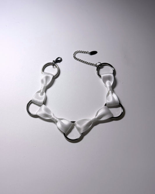 A white satin bow collar with silver metal O-rings and a silver chain extender, displayed on a light gray background.