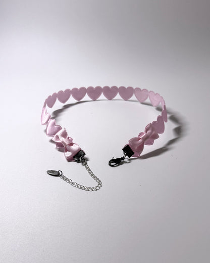 A light pink heart-patterned choker collar with a silver lobster clasp and an adjustable silver chain extender, displayed on a neutral light gray background.
