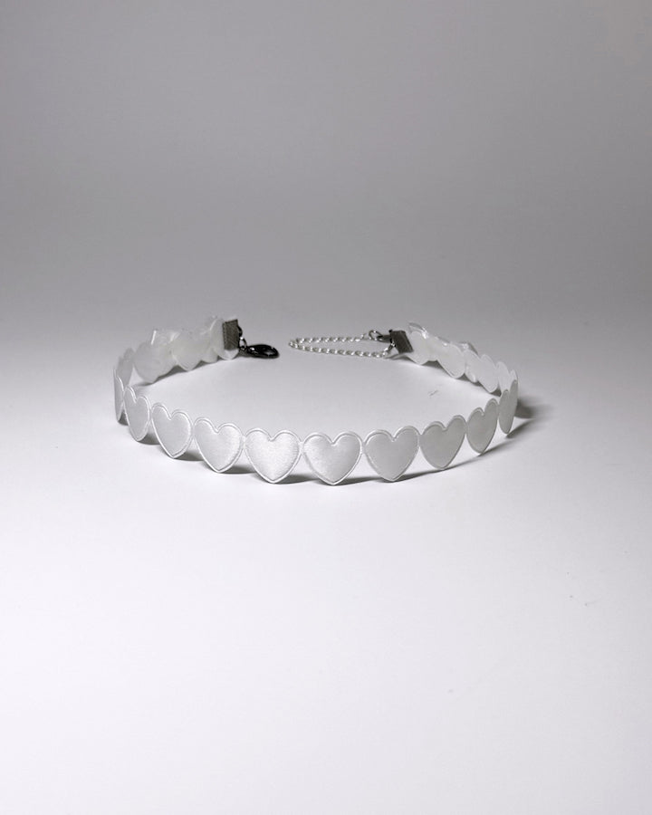 A white heart collar with a silver metal chain extender, photographed on a neutral light gray background.