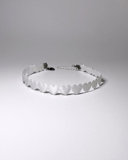 A white heart collar with a silver metal chain extender, photographed on a neutral light gray background.