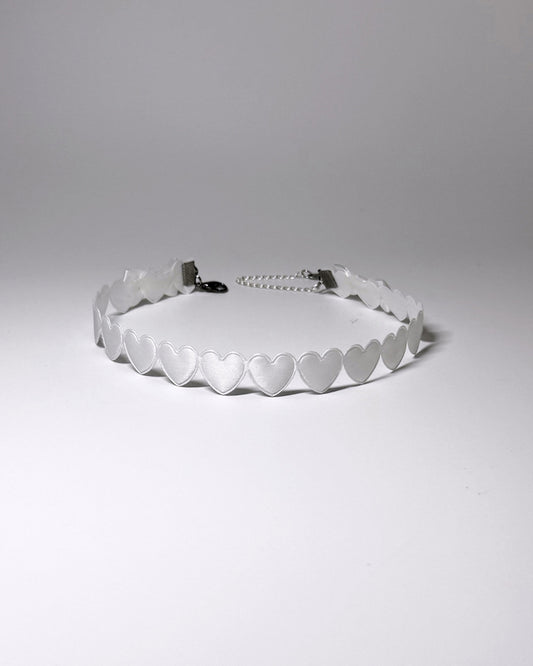 A white heart collar with a silver metal chain extender, photographed on a neutral light gray background.