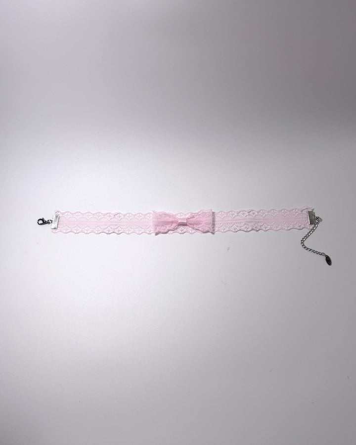 A light pink lace garter bow choker with a silver-tone chain extender with clasp, laid flat on a light gray background.