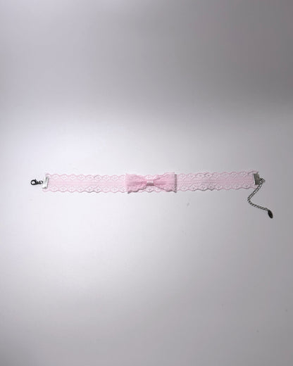 A light pink lace garter bow choker with a silver-tone chain extender with clasp, laid flat on a light gray background.