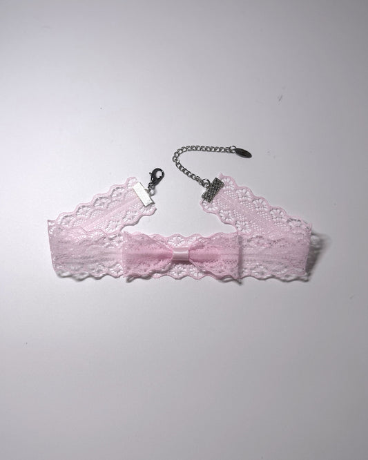A light pink lace garter bow choker with a silver-tone chain extender with clasp, laid flat on a light gray background.