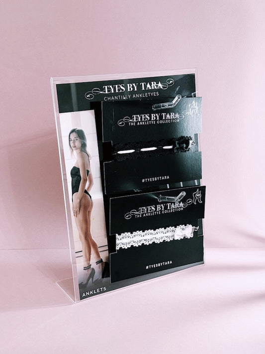 Tyes by Tara product display stand with jewelry packaging on a pink background