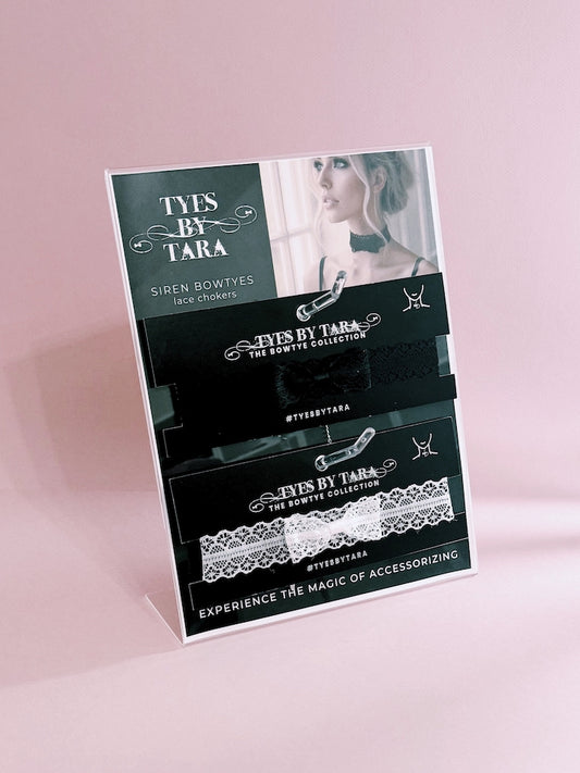 Product display stand with 'Tyes by Tara' lace bowties on a pink background