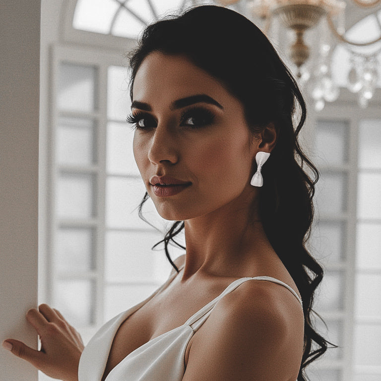 White Bow Earrings on Brunette Model in White Dress under Chandelier