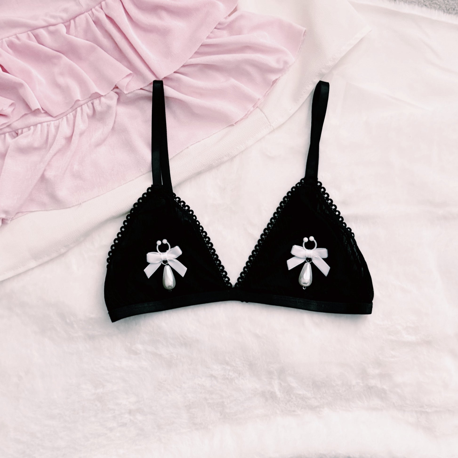 Black bra with white bow nipple clamps jewelry on a pink and white background