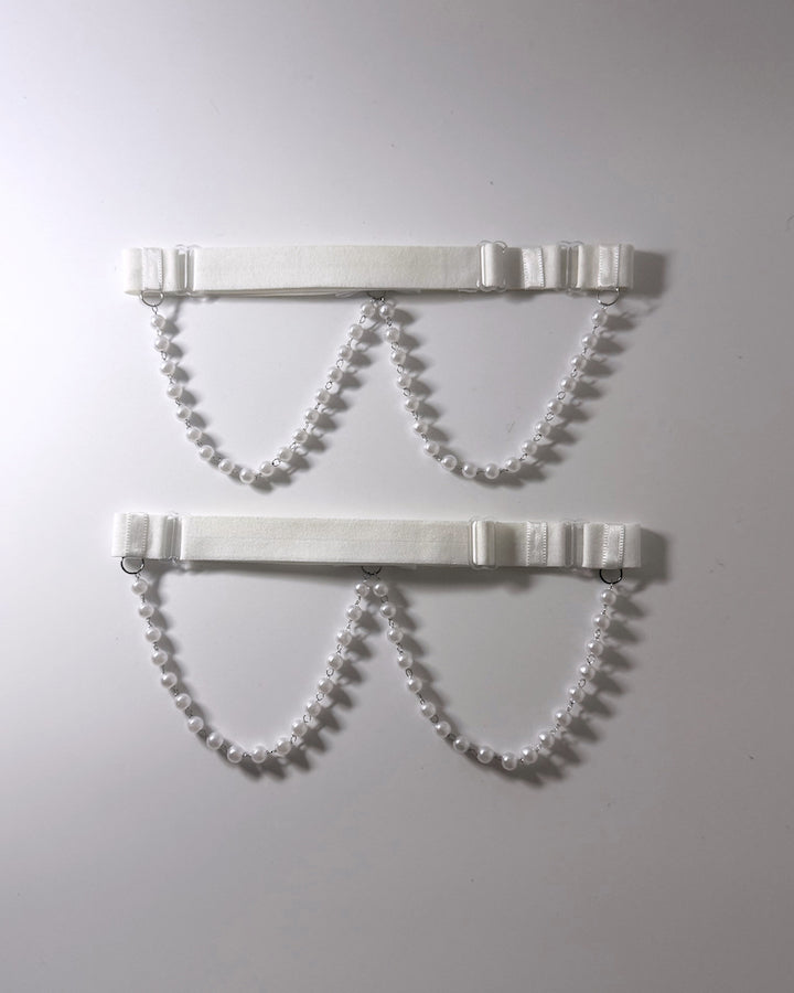 White Pearl Leg Garters Two white elastic  garters with pearl bead chains and small white bows, displayed against a plain light gray background showing the adjustable elastic straps
