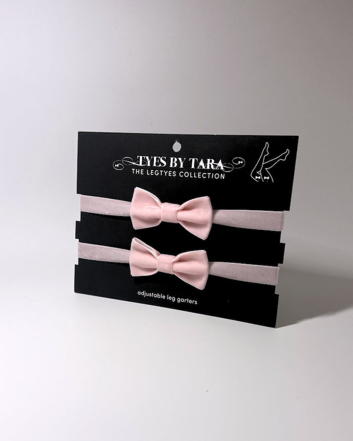 pink velvet bow leg garters displayed on a black card