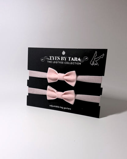 pink velvet bow leg garters displayed on a black card
