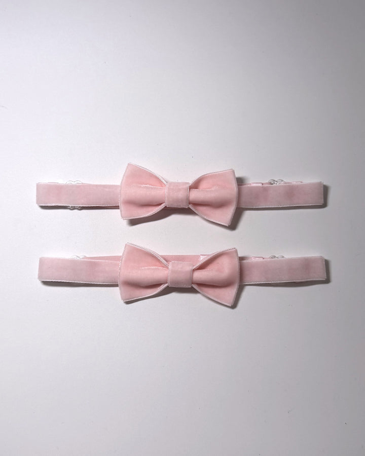 Two light pink velvet bow leg garters with matching elastic bands, arranged vertically on a plain white background.