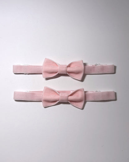 Two light pink velvet bow leg garters with matching elastic bands, arranged vertically on a plain white background.
