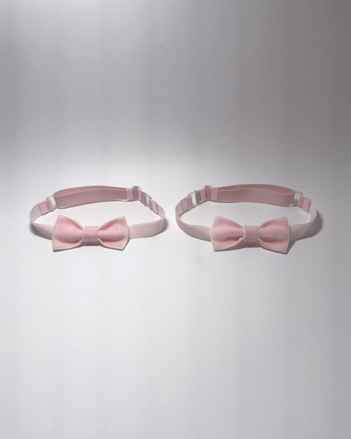 Two light pink bow velvet leg garters with adjustable elastic straps, displayed side-by-side on a light gray background.